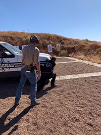 Man seeking cover behind a vehicle while firing on targets during a training exercise.